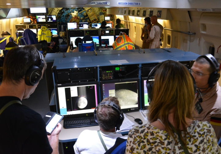Lehrkräfte im Gespräch mit DSI-Ingenieur Oliver Zeile an ihrer Computerkonsole verfolgen die Messungen des Wassergehalts auf der Mondoberfläche – im Hintergrund die Innenansicht des SOFIA-Observatoriums. 